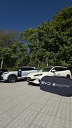 Zwei Elektroautos der Marke BYD stehen nebeneinander auf einem gepflasterten Parkplatz vor grünen Bäumen, davor ein schwarzes Werbebanner mit den Logos von BYD und Schreiner & Wöllenstein