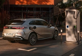 Silberner Mercedes-Benz GLC EQ SUV lädt an einer Ladestation vor modernem Gebäude mit vertikalen Holzlamellen bei Sonnenuntergang.