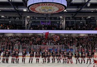Eishockeyspieler beider Teams stehen auf dem Eis vor einer vollen Tribüne, darüber hängt eine Anzeigetafel mit dem Spielstand 4:2.
