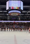 Eishockeyspieler beider Teams stehen auf dem Eis vor einer vollen Tribüne, darüber hängt eine Anzeigetafel mit dem Spielstand 4:2.