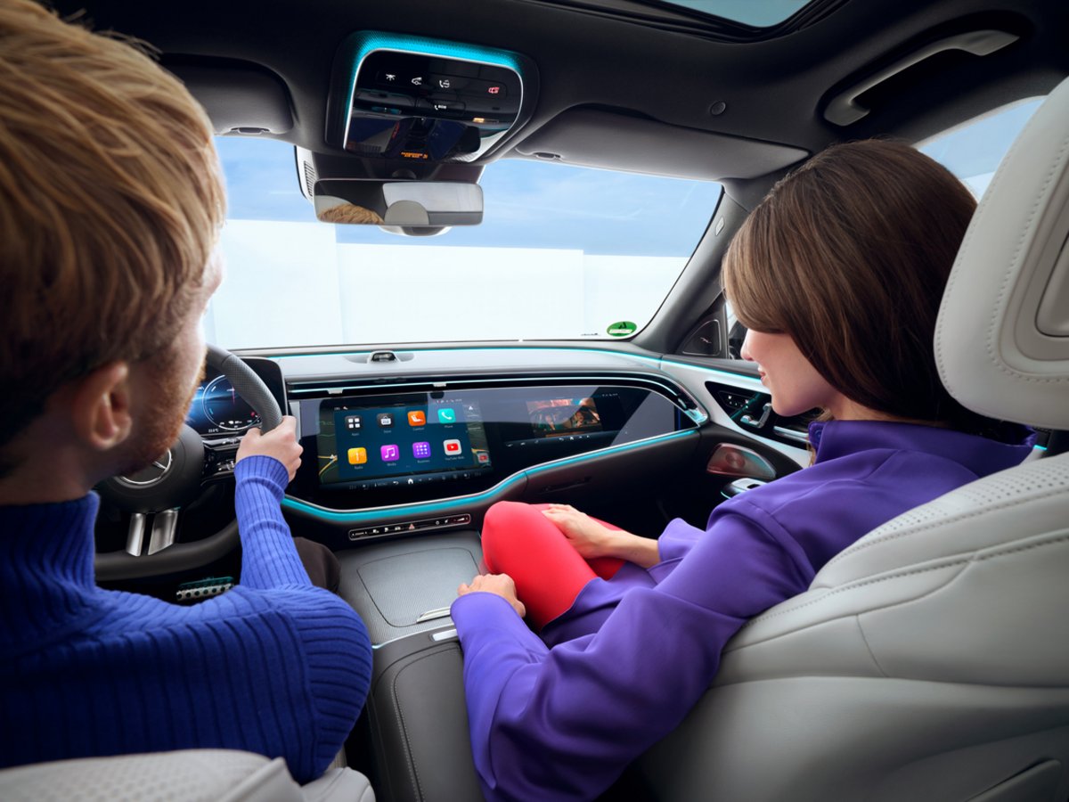 Fahrer und Beifahrerin im Mercedes-Benz mit großem Superscreen für Videostreaming und Infotainment im Innenraum.