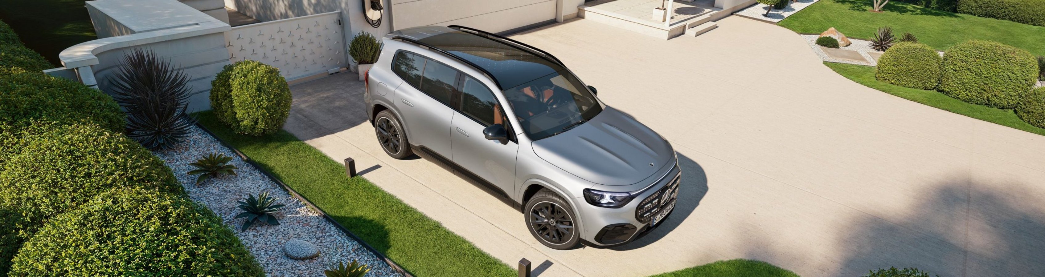 Moderner SUV steht vor einem zweistöckigen Haus mit Garage, umgeben von gepflegtem Garten mit runden Hecken und Kiesweg.