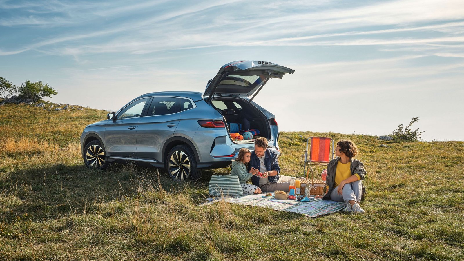 BYD SEAL U SUV in Silber steht auf einer Wiese mit geöffnetem Kofferraum, zwei Personen sitzen auf einer Decke und machen Picknick