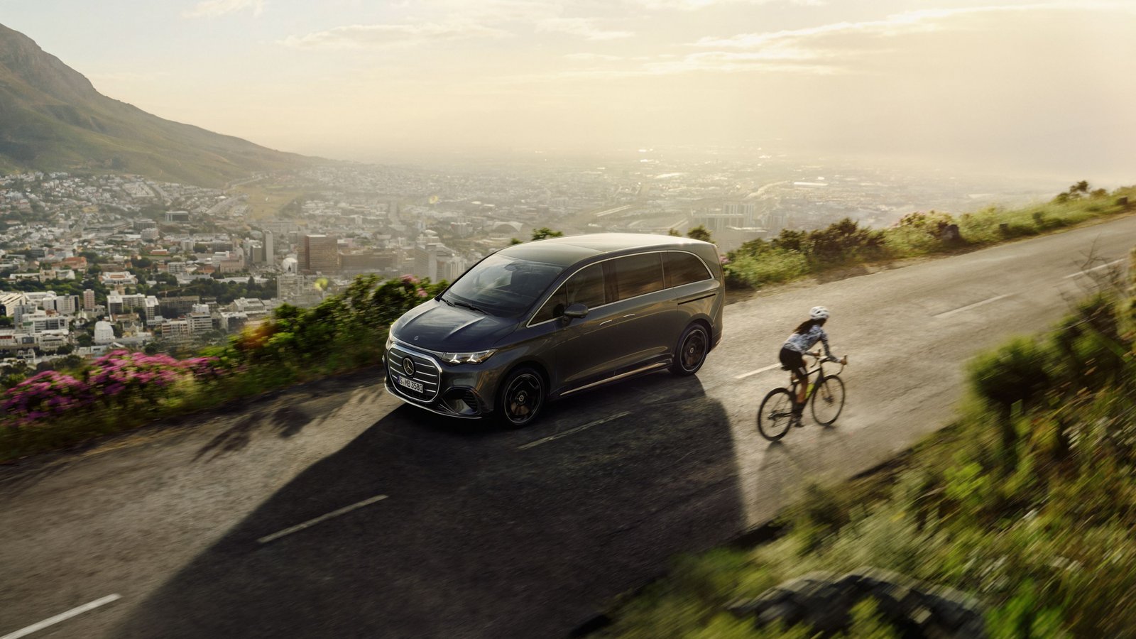 Mercedes-Benz VLE fährt auf einer Bergstraße mit Blick auf eine Stadt, neben einem Radfahrer