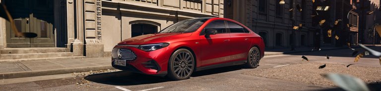 Neuer Mercedes-Benz CLA 250+ in Rot seitlich aufgenommen vor historischer Stadtkulisse mit modernen Designelementen.